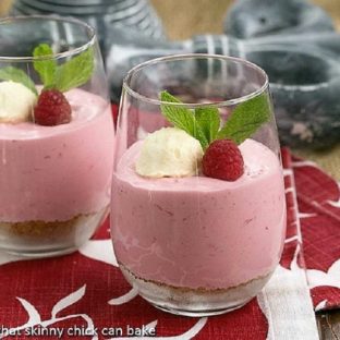 Raspberry Mousse in parfait glasses topped with whipped cream, fresh raspberries and mint