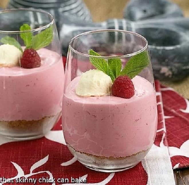 Raspberry Mousse in parfait glasses topped with whipped cream, fresh raspberries and mint
