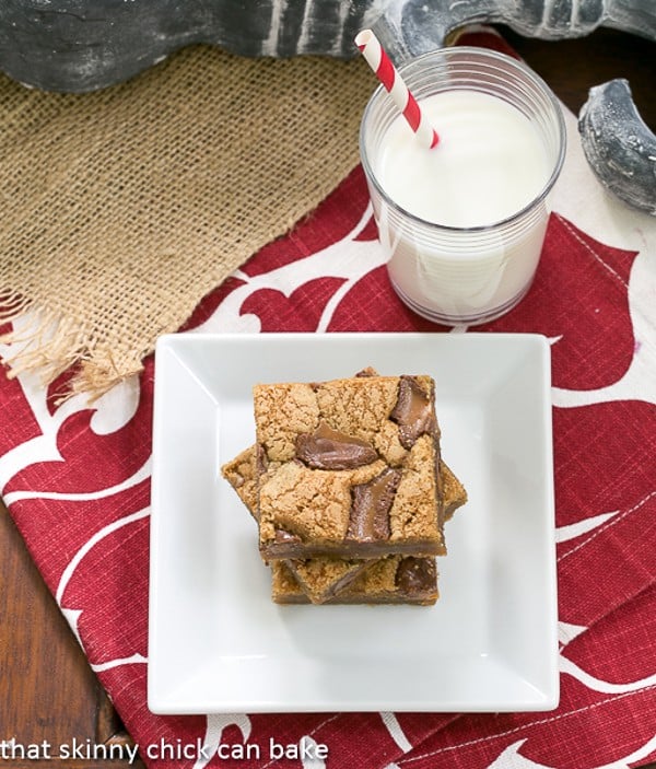 Biscoff Rolo Bars stacked on a square white plate with a glass of milk