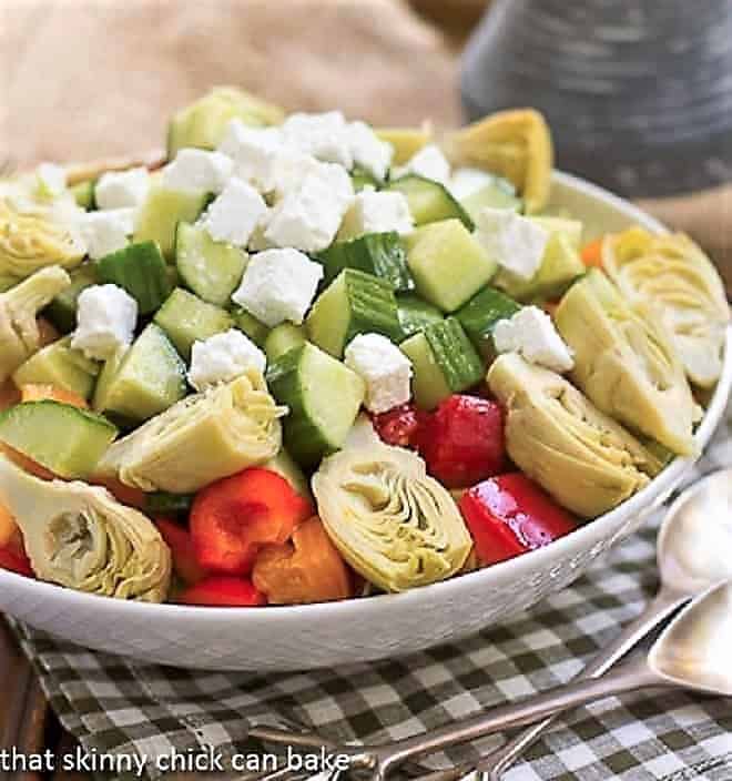 Greek Salad with Feta in a white salad bowl with silver serving spoon and fork.