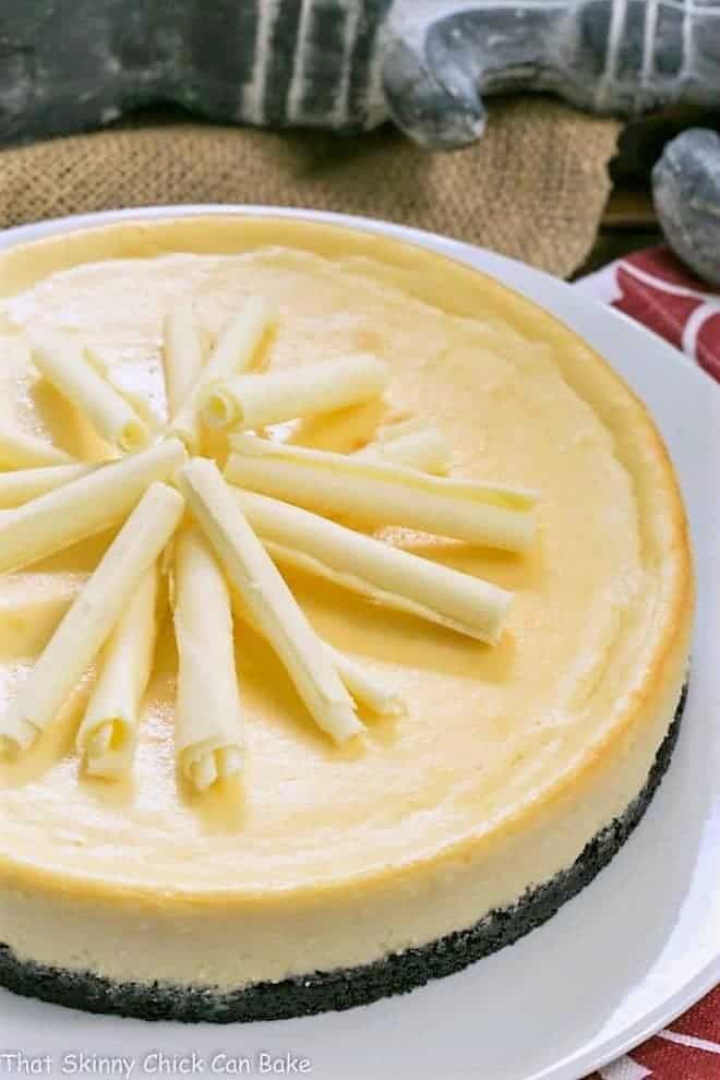 White Chocolate Frangelico Cheesecake garnished with white chocolate curls on a white cake plate.