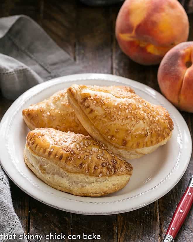 Peach Hand pies on a round white plate with a red handled fork.