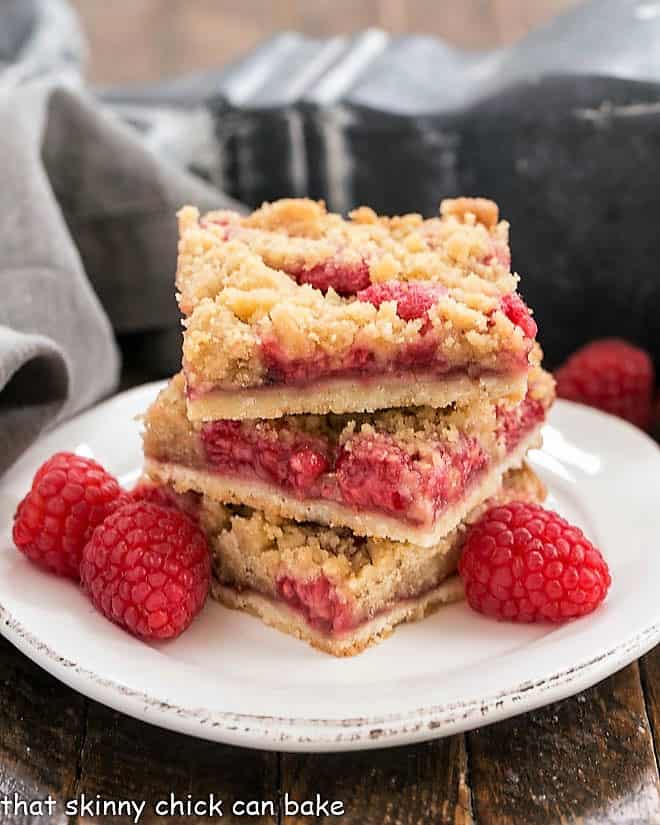 Streusel Topped Raspberry Squares stacked on a small plate with fresh raspberries.