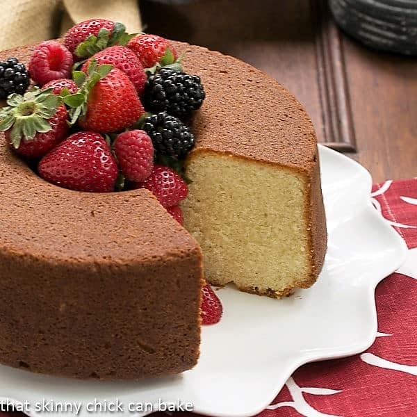  Whole Vanilla Pound Cake on a white platter with a slice removed and berries piled in the middle.