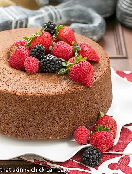 Whole Vanilla Pound Cake on a white ruffled plate topped with berries.