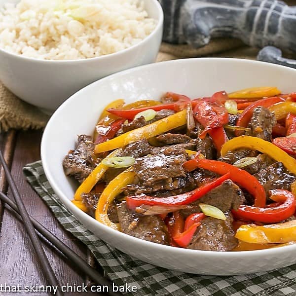 Asian Beef with Peppers in a white serving bowl with a side dish of rice