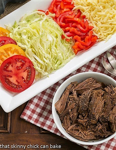 Overhead view of Slow Cooker Beef Barbacoa in a white bowl with toppings on a white tray.
