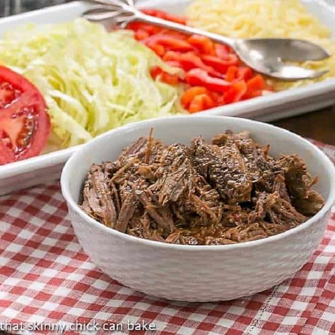 Slow Cooker Beef Barbacoa shredded in front of a white tray of toppings