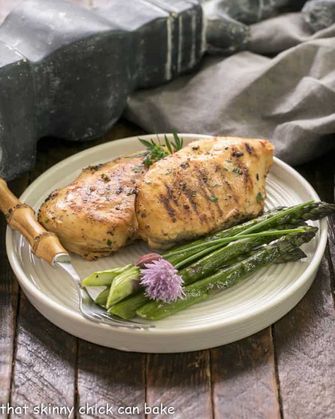 2 chicken breasts on a dinner plate with asparagus spears and a bamboo handle fork.