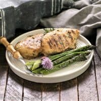 Mustard garlic lime marinated chicken on a white dinner plate with asparagus spears and a fork