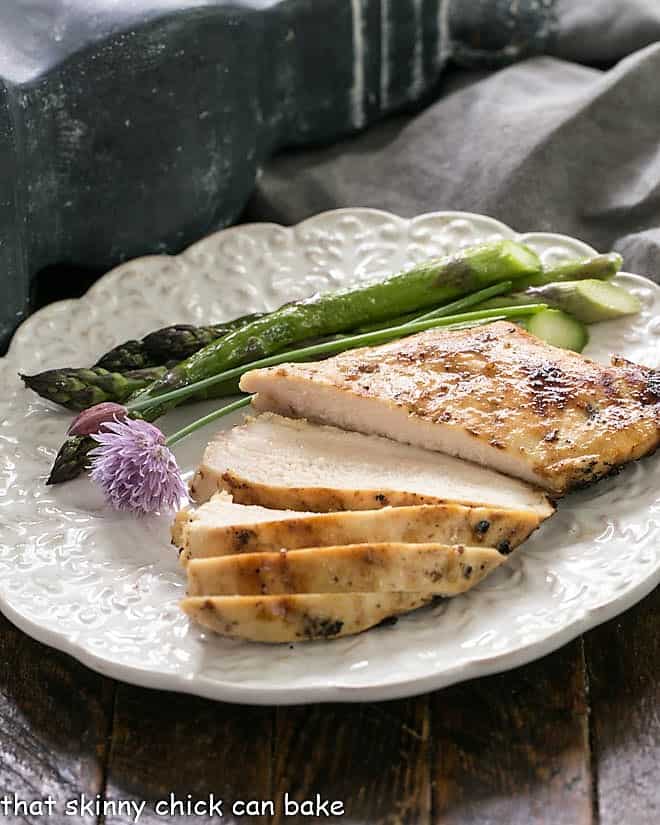 A sliced chicken breast on a white dinner plate with asparagus.