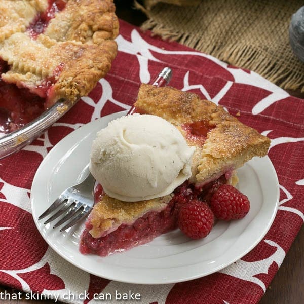 Lattice Topped Raspberry Pie on a white plate with a  scoop of vanilla ice cream and a fork.