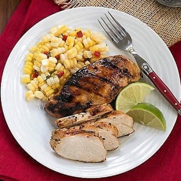 Overhead view of marinated chicken and sides on a white dinner plate with a fork and lime wedges.