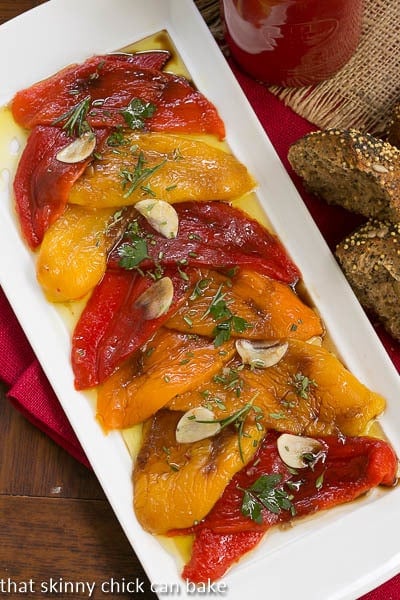 Overhead view of Oven Roasted Peppers with garlic slices and herbs on a white platter.