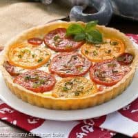 Summer tomato tart on a white plate garnished with a sprig of fresh basil