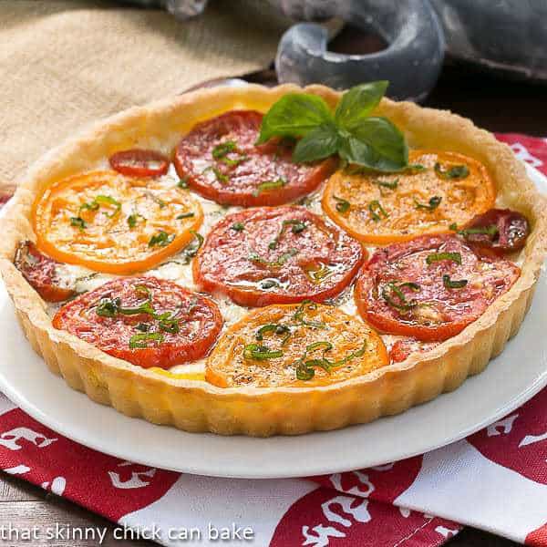 Summer Tomato Tart on a white serving plate garnished with a sprig of basil