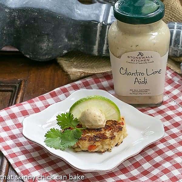 Crab Cakes on a square white plate with aioli, a lime slice and cilantro