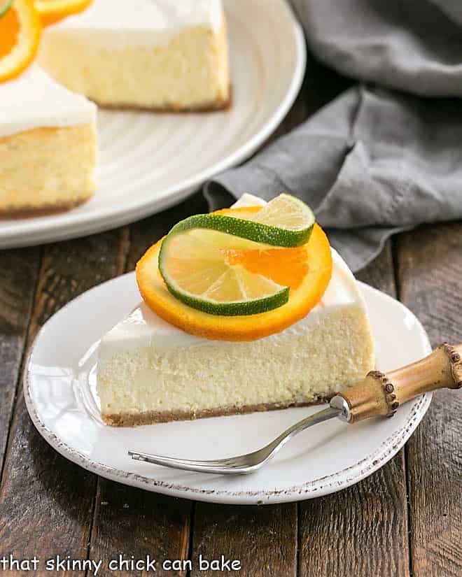  Margarita Cheesecake slice on a white dessert plate garnished with an orange and lime slice