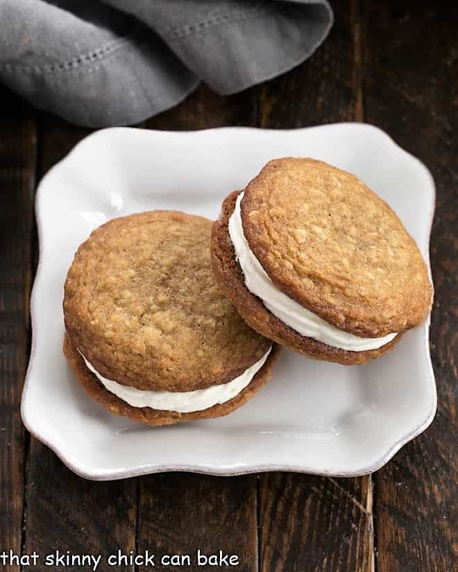 Copycat Litte Debbie Oatmeal Creme Pies - Better than Little Debbies!!! Big, chewy oatmeal cookies with a dreamy cream filling. Overhead view of 2 Oatmeal Creme Pies on a square white plate.