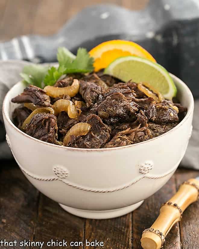 Vaca Frita in a white bowl over rice and garnished with tomatoes and orange and lime slices.