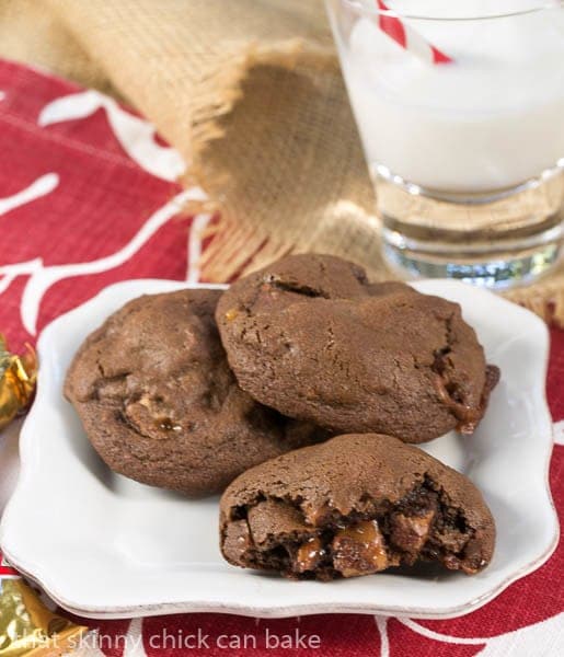 Double Chocolate Twix Cookies on a white plate with one broken open to reveal the candy filled interior