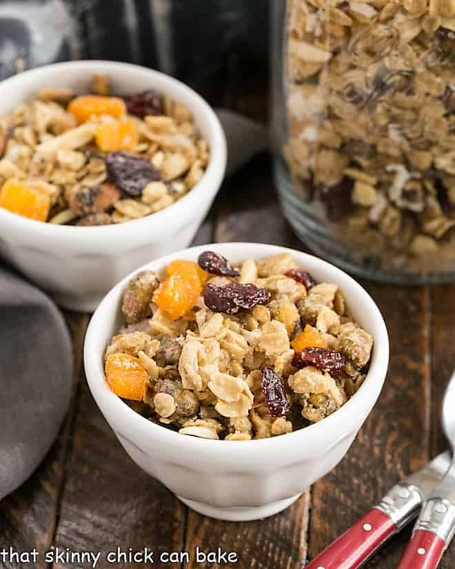 Pistachio Coconut Granola in 2 white cereal bowls with 2 red handled spoons