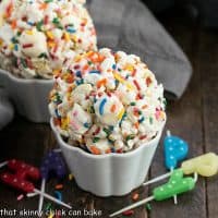 Two popcorn balls in white ramekins surrounded by colorful candles