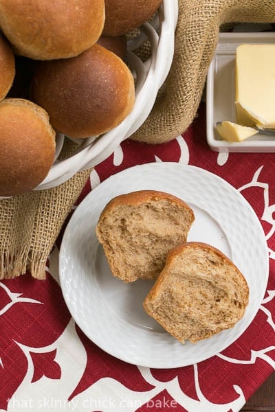 Whole Wheat Dinner Rolls in a basket and one cut open on a white plate.