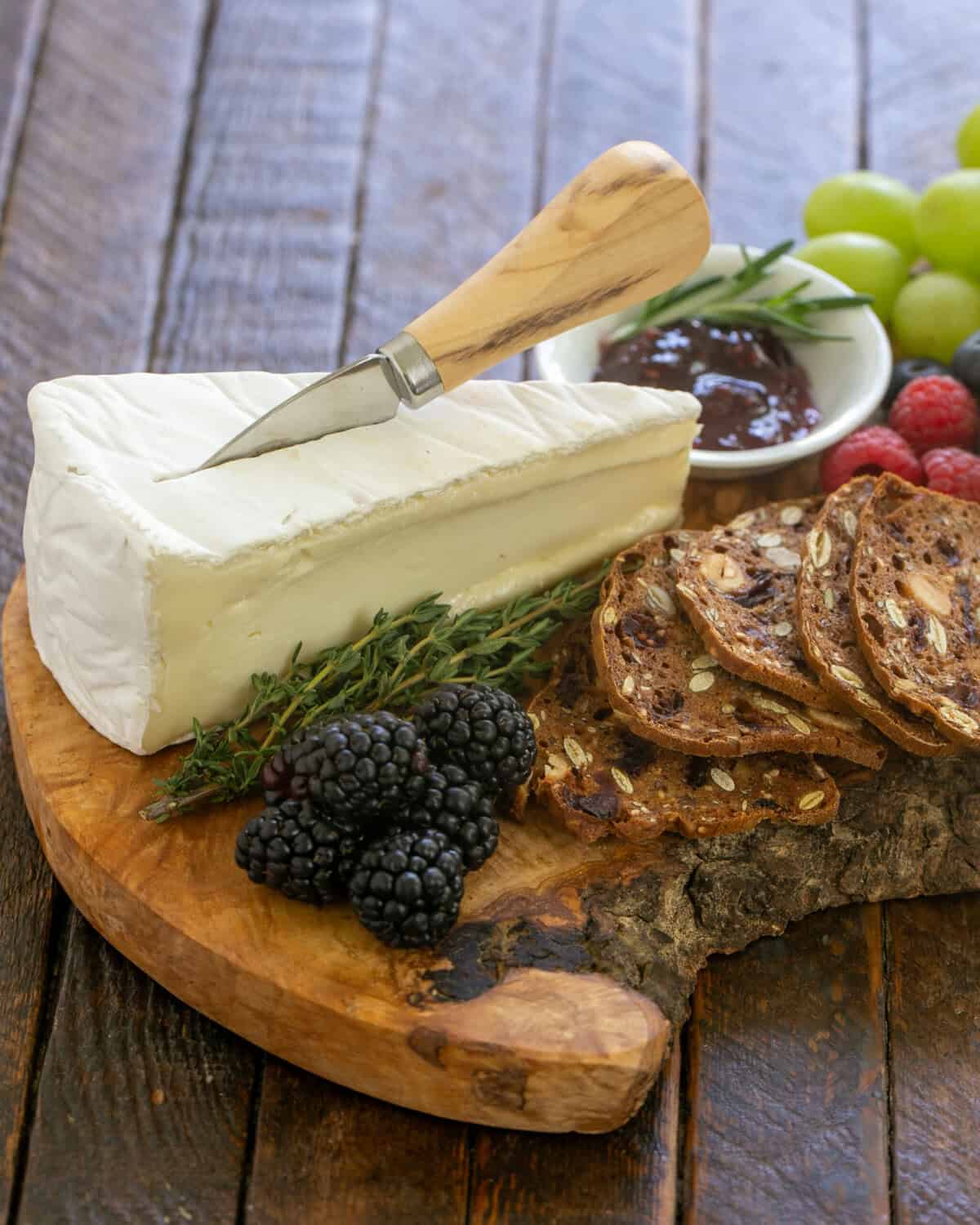 Brie with crackers and fruit on a beautiful wooden cheese board.