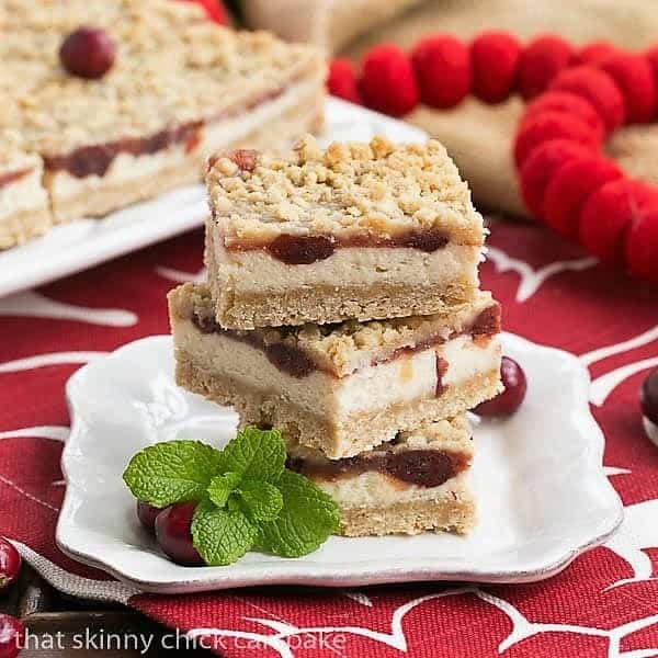 A stack of 3 cranberry cheesecake bars on a square white plate