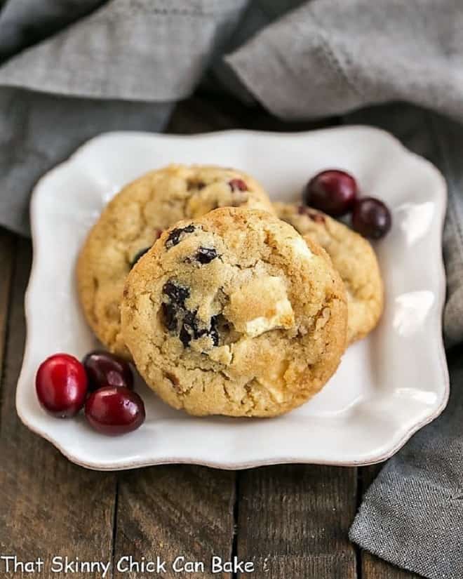 Cranberry, White Chocolate, Crystallized Ginger Cookies on a square white plate with fresh cranberries.