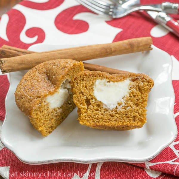 Cream Cheese Filled Pumpkin Muffin cut in half on a small white plate garnished with cinnamon sticks