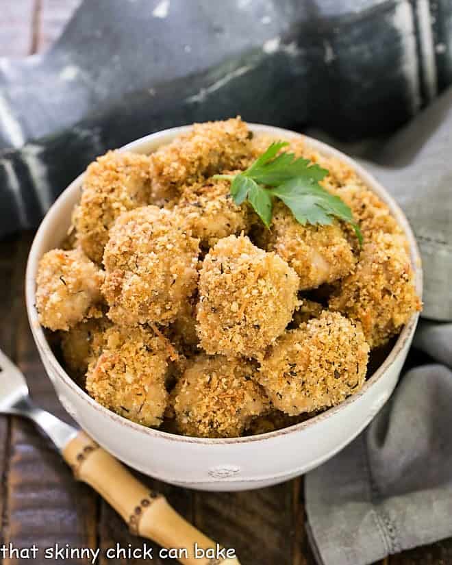 Overhead view of Herbed Chicken Nuggets in a white bowl with a sprig of parsley and a bamboo handle fork