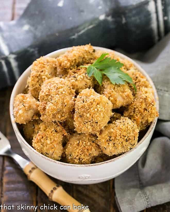 Overhead view of Herbed Chicken Nuggets in a white bowl with a sprig of parsley and a bamboo handle fork.