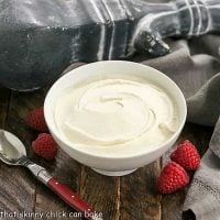 Homemade Mascarpone Cheese in a white bowl with fresh raspberries and a red handled spoon