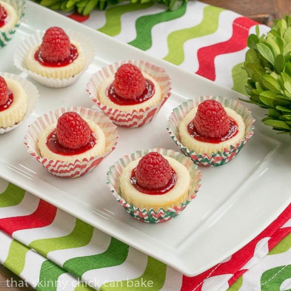 Mini Mascarpone Cheesecakes on a white tray topped with raspberry sauce and raspberries