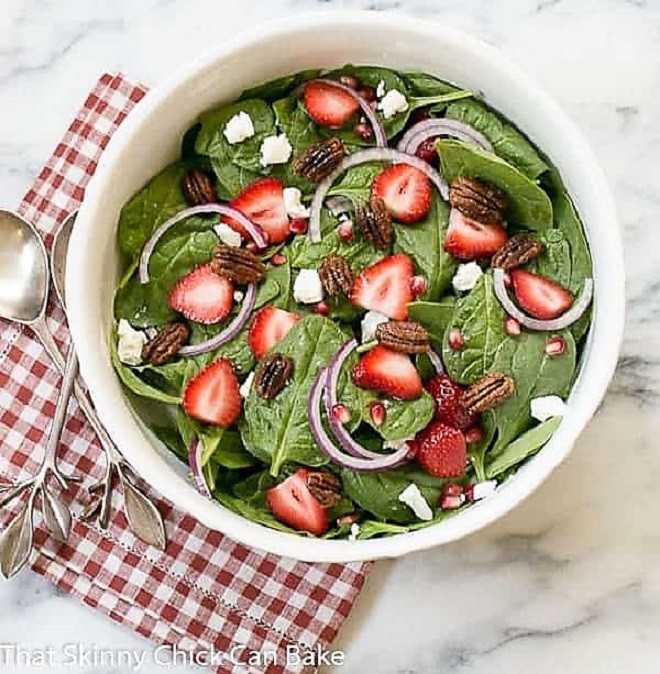 Spinach Strawberry Pomegranate Salad in a serving bowl over a red and white checked napkin.