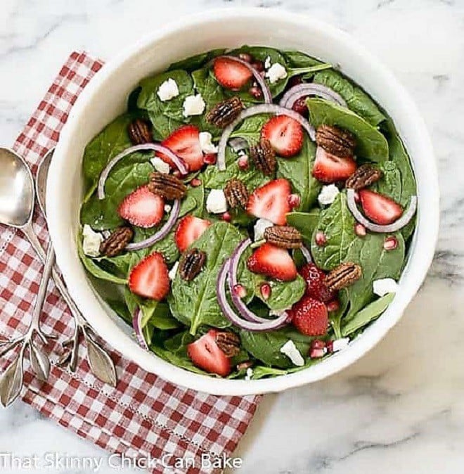 Spinach Strawberry Pomegranate Salad in a serving bowl over a red and white checked napkin.