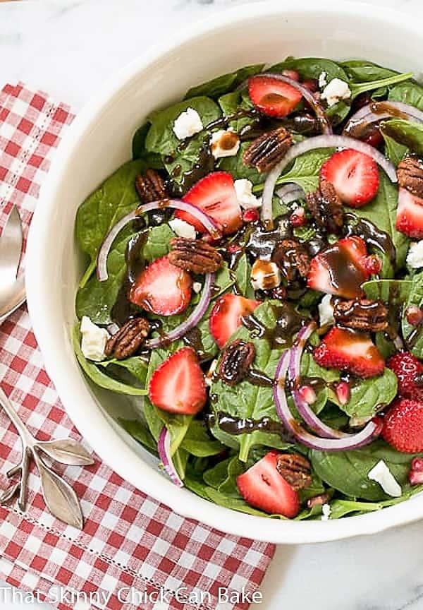 Spinach, Strawberry, Pomegranate, Feta Salad drizzled with a vinaigrette in a white ceramic serving bowl