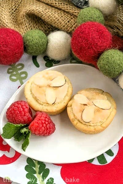 2 Almond Raspberry Tartlets on an oval plate garnished with berries and mint.