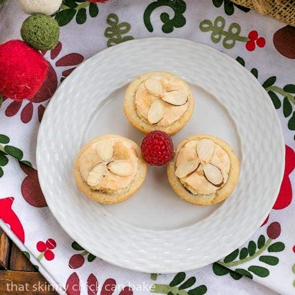 3 Almond Raspberry Tartlets on a white plate with a raspberry garnish.