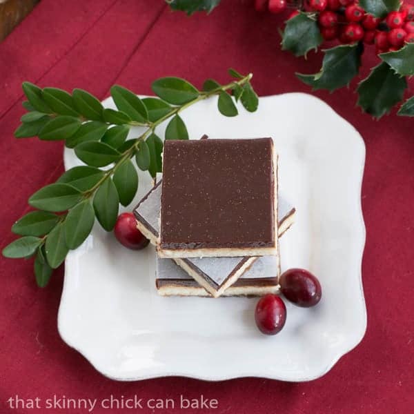 Ganache Topped Cheesecake Bars stacked on a white plate with cranberries and boxwood to garnish.