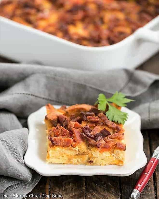 Easy Bacon and Egg Strata slice on a white plate in front of the strata in a casserole dish.