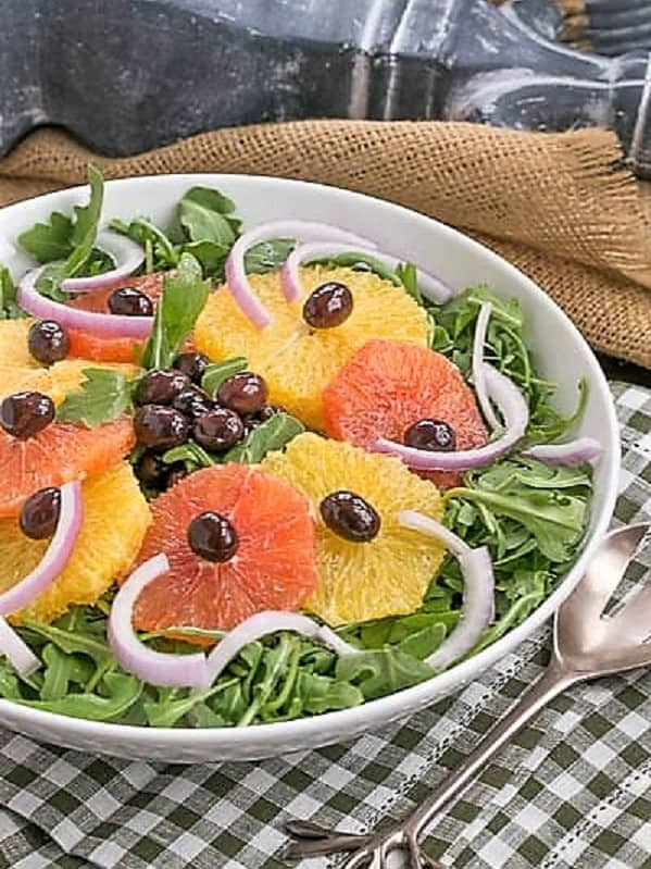 Orange Olive Moroccan Salad on a bed of arugula in a white bowl on a checked napkin.