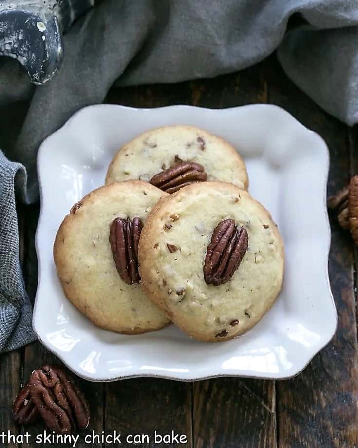 Overhead view of 3 pecan sandies on a square white decorative plate.