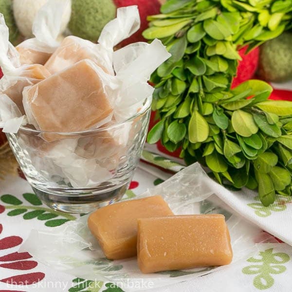  Two unwrapped Soft Vanilla Caramels in front of a glass bowl of caramels