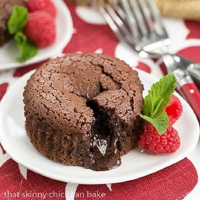 Chocolate Lava Cakes broken open on a white plate with raspberries and mint.