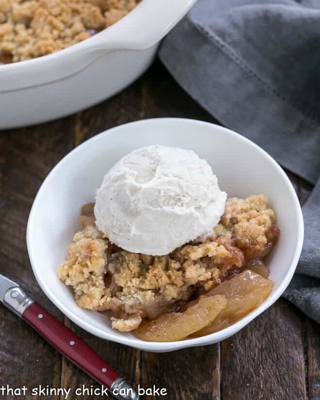 Serving of Easy Apple Crisp in a small white bowl with a scoop of vanilla ice cream