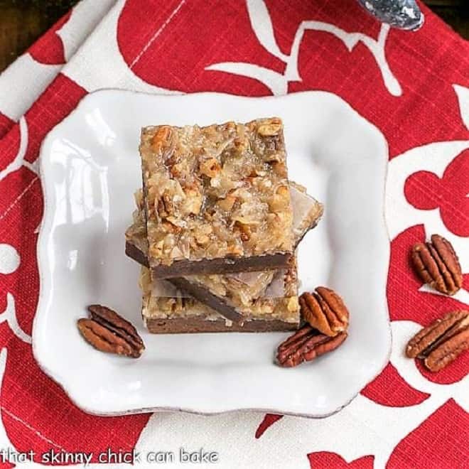 Overhead view of a stack of German Chocolate Brownies on a square white plate with pecan halves.