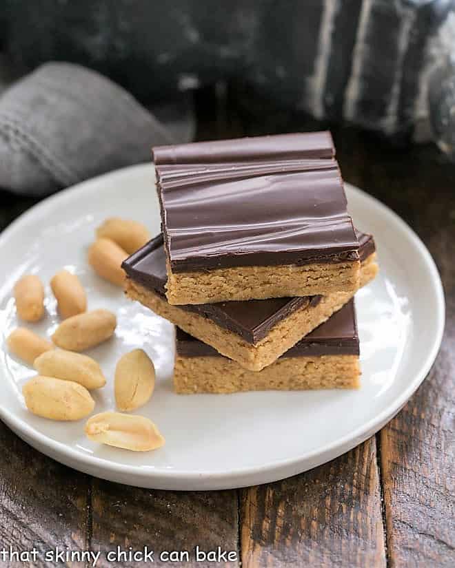 Homemade Reese's Bars stacked on a roung plate with shelled peanuts.